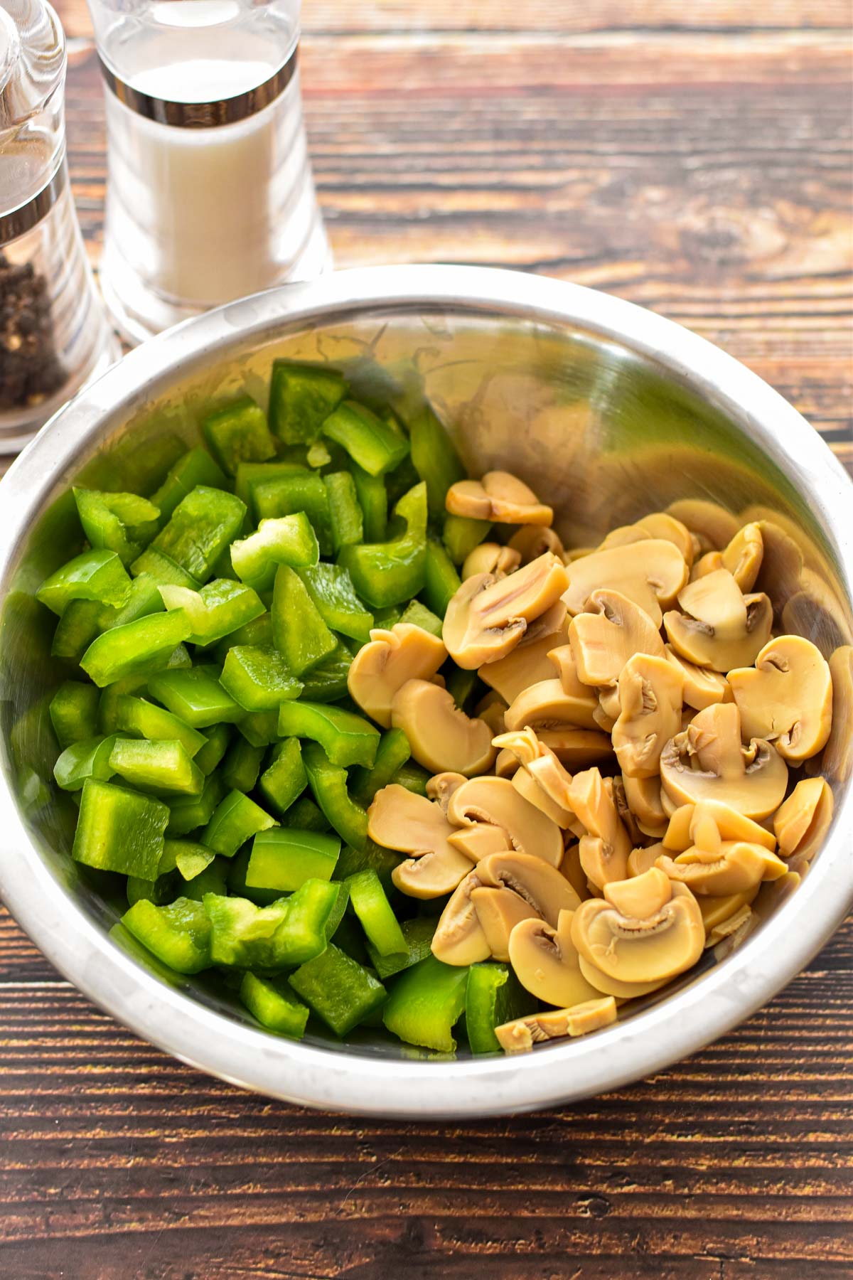 process shot of diced green bell pepper and sliced canned mushrooms in a mixing bowl in front of salt and pepper shakers