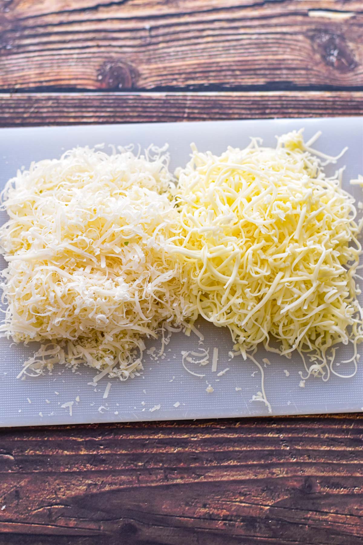 process shot of shredded mozzarella and parmesan cheese on a white cutting board
