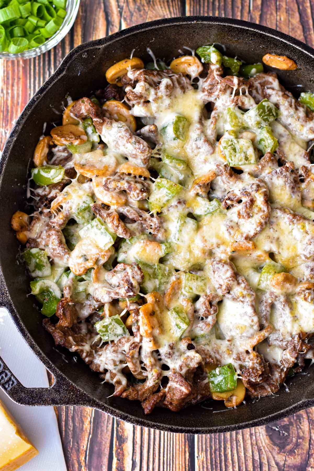 overhead shot of low fodmap philly cheesesteak skillet dinner next to a white cutting board with parmesan cheese and a bowl of chopped scallions