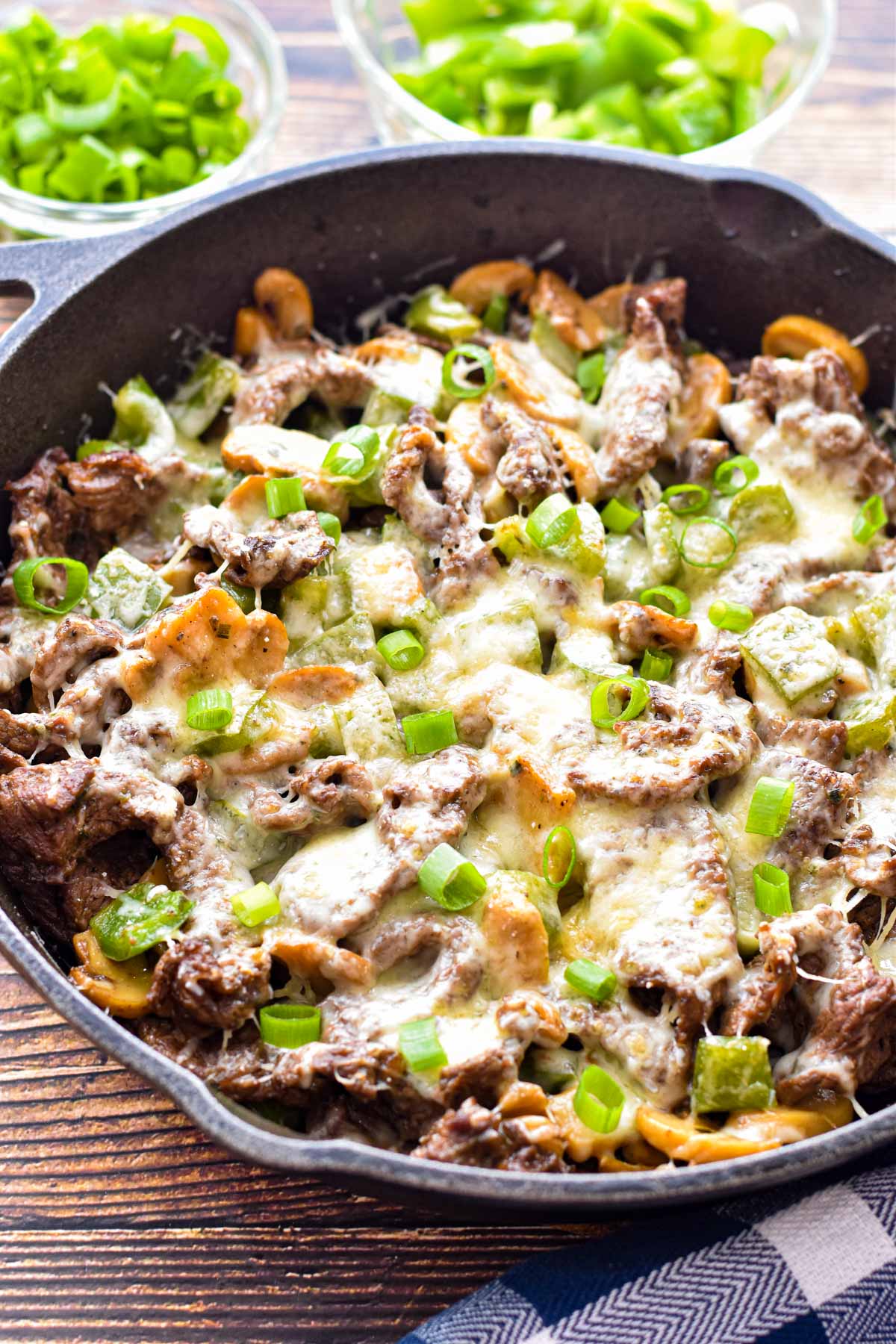 side angle shot of low fodmap philly cheesesteak skillet in front of bowls of chopped scallions and green bell pepper