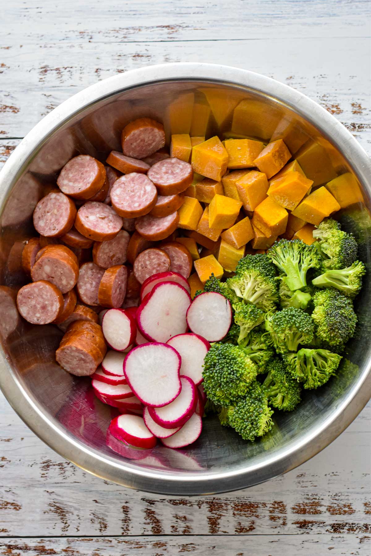 process shot of sliced low fodmap sausage and chopped fall vegetables including kabocha squash, broccoli and radish in a large mixing bowl