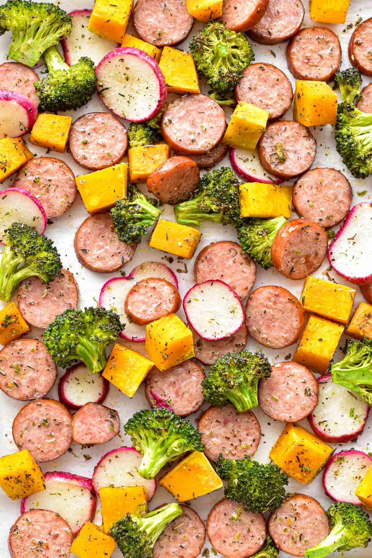 close up overhead shot of roasted low fodmap sausage and fall vegetables on white parchment paper