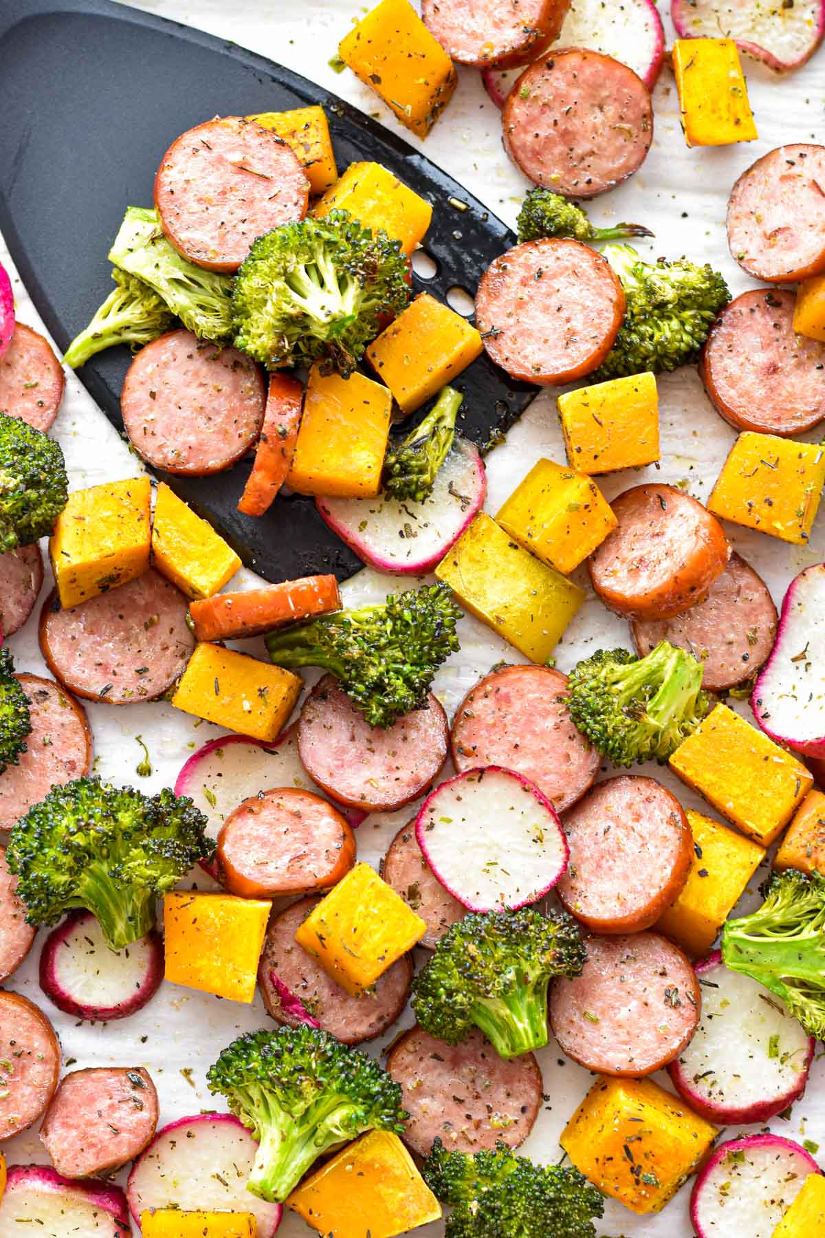 roasted low fodmap smoked sausage and vegetables on parchment paper with a black spatula
