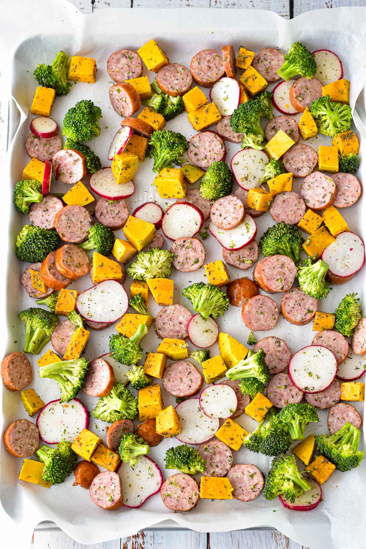 process shot of low fodmap sausage and vegetables on a sheet pan covered in parchment paper prior to cooking
