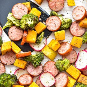low fodmap sausage and fall vegetables on parchment paper with a black spatula