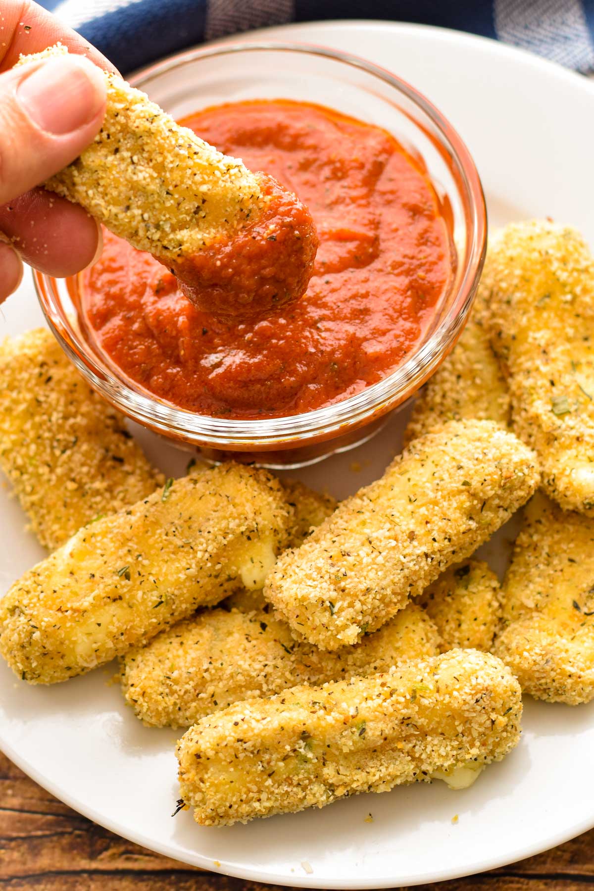 dipping a low fodmap mozzarella stick into a bowl of tomato sauce on a white plate