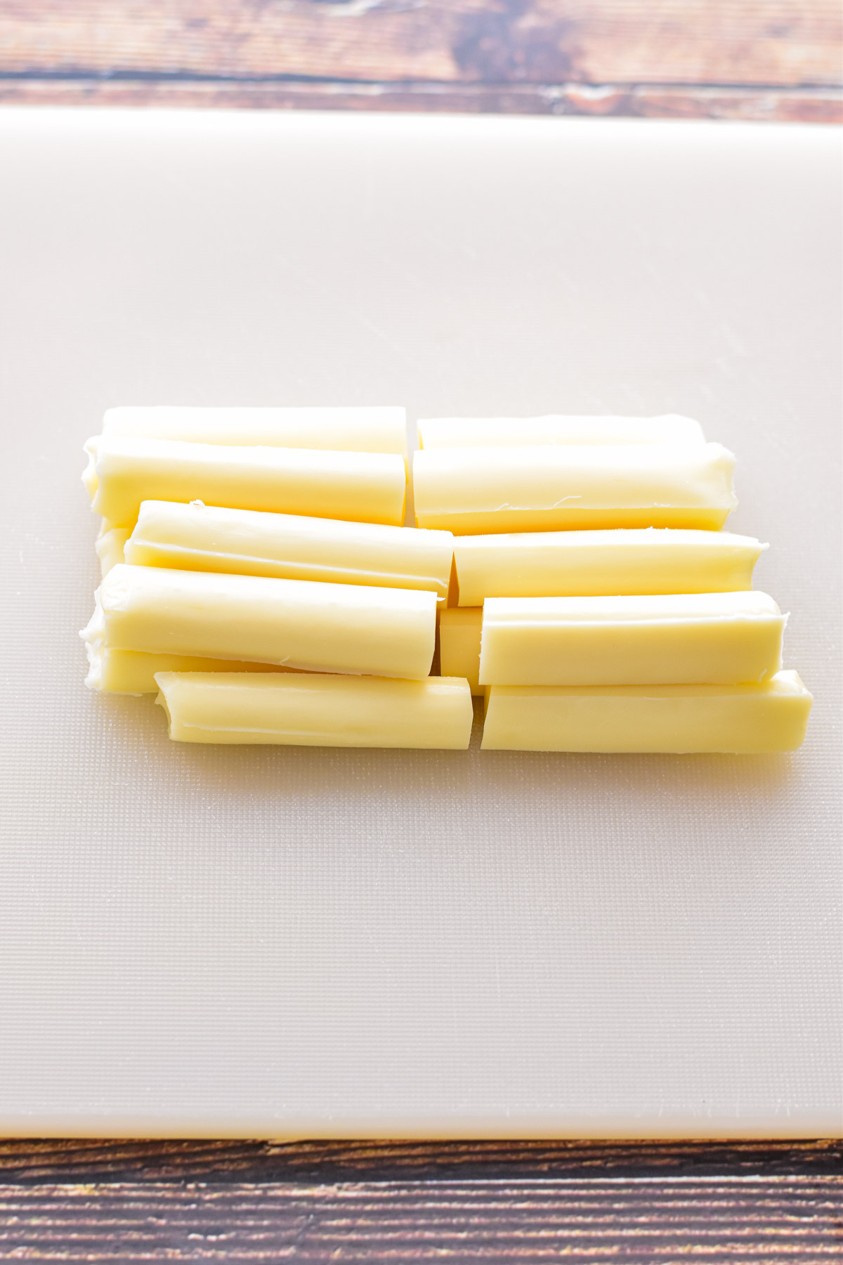 process shot of mozzarella string cheese sticks cut in half on a white chopping board