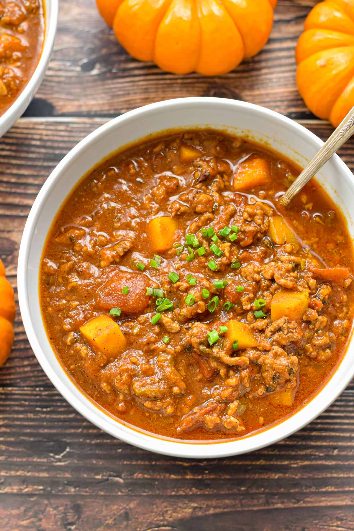 close up shot of low fodmap double pumpkin chili in a white bowl with a spoon on a brown wooden background