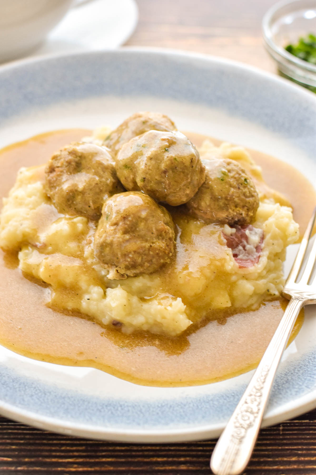 low fodmap meatballs and mashed potatoes covered in gravy on a blue and white plate with a fork