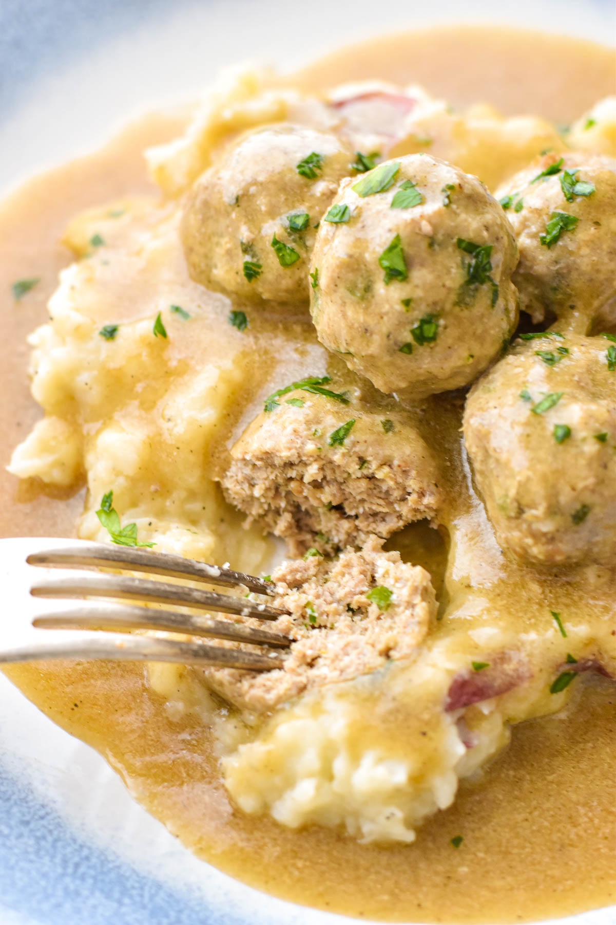 close up of a fork cutting into low fodmap turkey meatballs on top of mashed potatoes covered in gravy