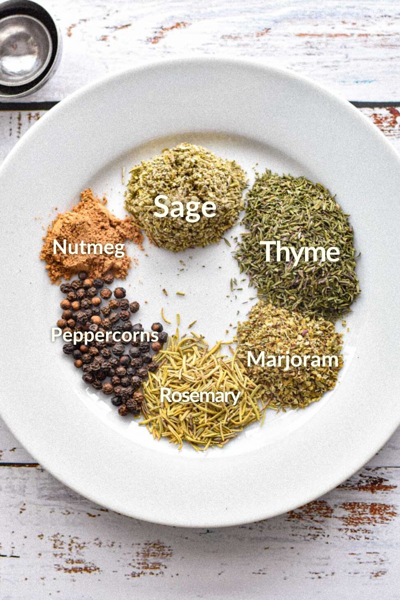 Low FODMAP poultry seasoning ingredients on a white plate, including sage, thyme, marjoram, rosemary, peppercorns, and nutmeg