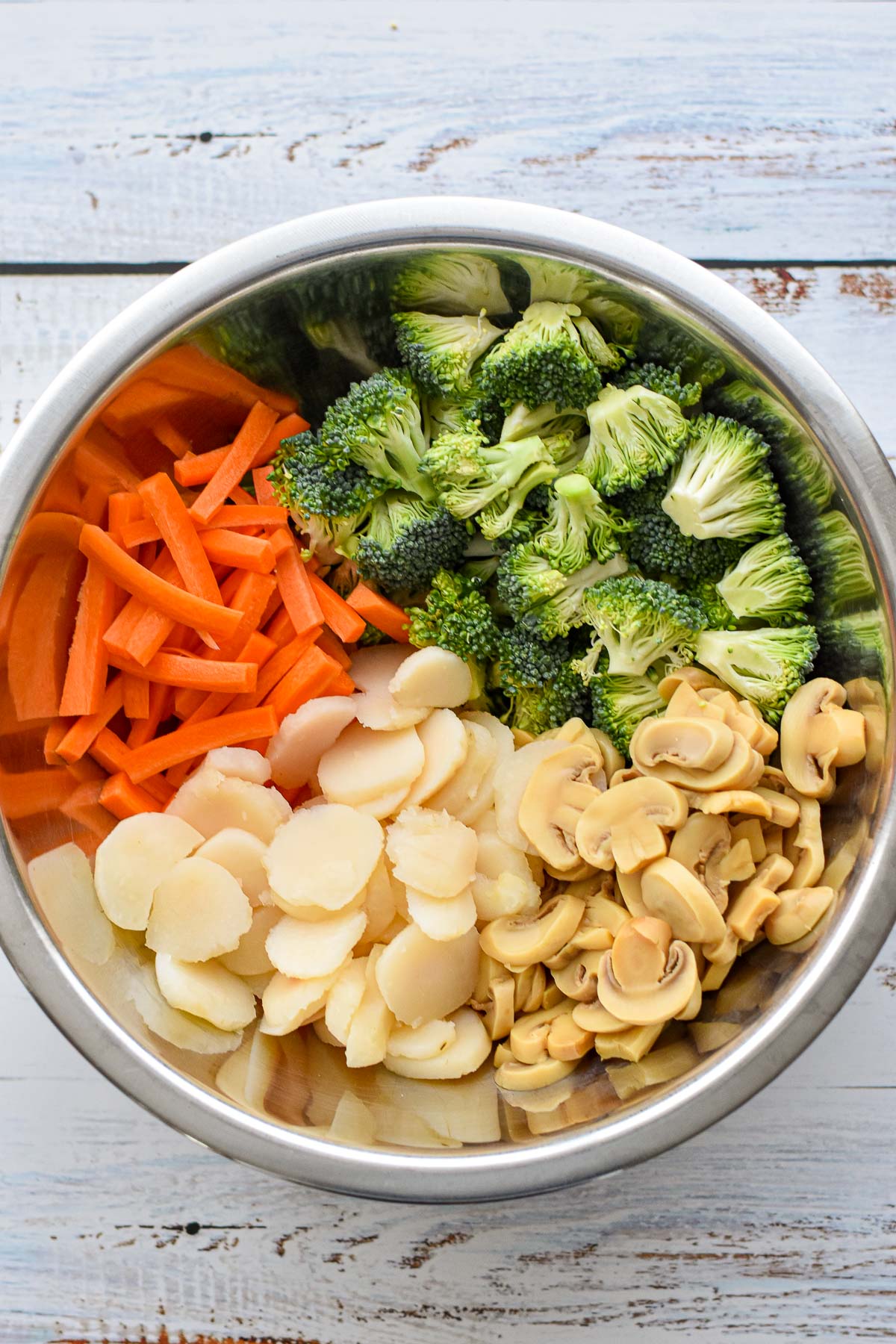 process shot of the veggies for low fodmap chicken stir fry including chopped broccoli heads, carrot matchsticks, and canned sliced water chestnuts and mushrooms