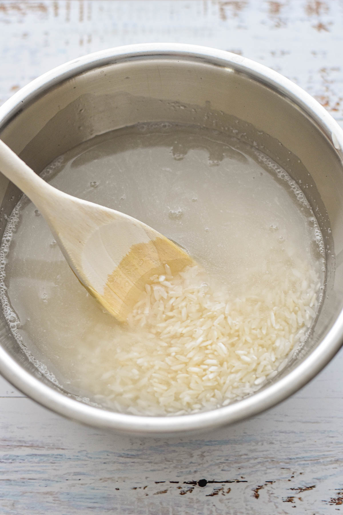 process shot of stirring long grain white rice in a stainless steel bowl with a spoon to make Instant Pot pot-in-pot rice