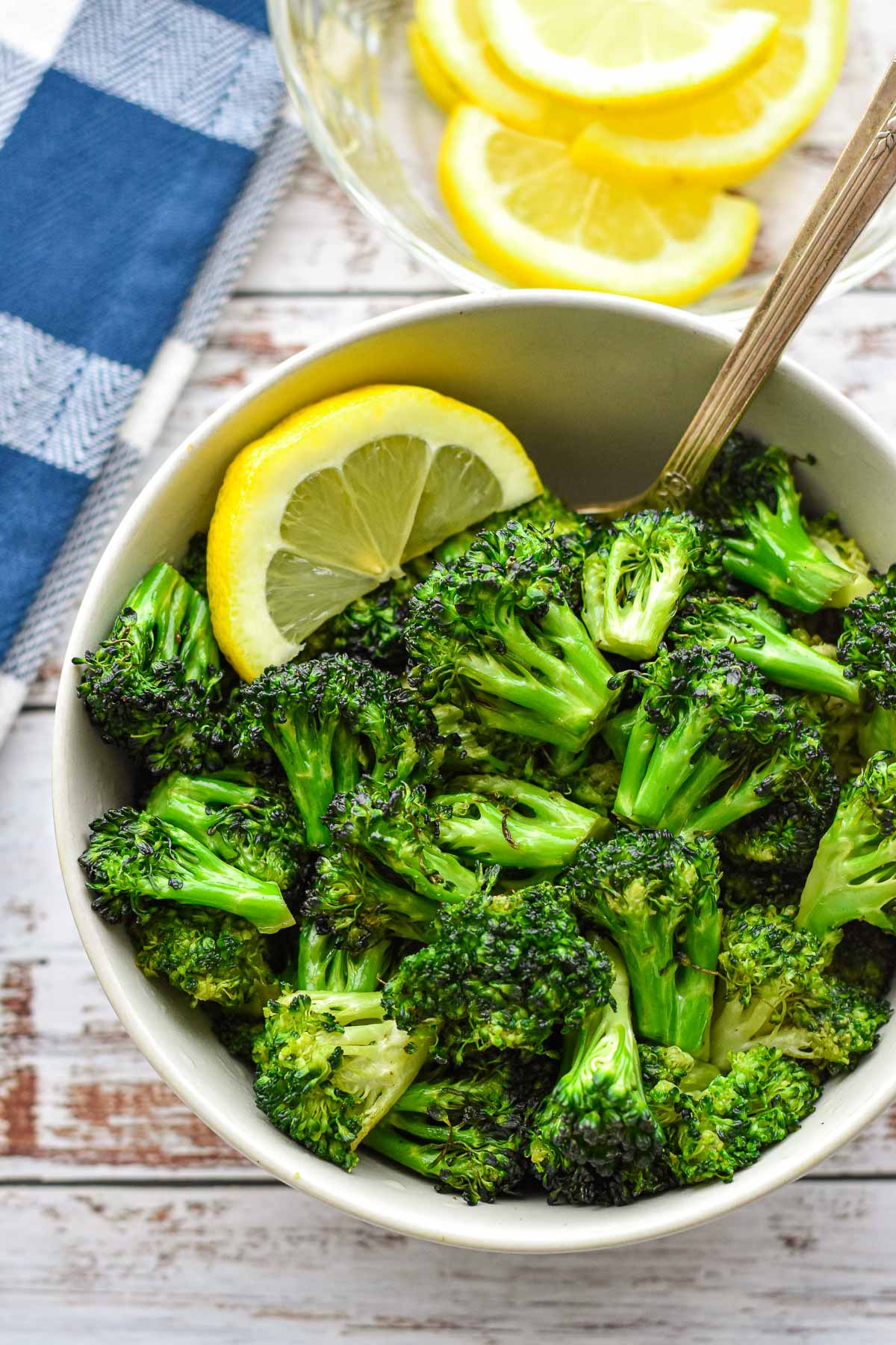 low fodmap air fryer broccoli in a white bowl with a spoon and lemon slice