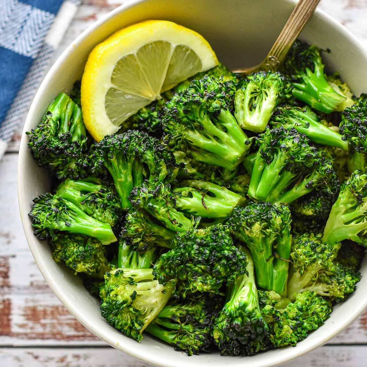 overhead shot of low fodmap air fryer broccoli in a white bowl with a spoon and lemon slice