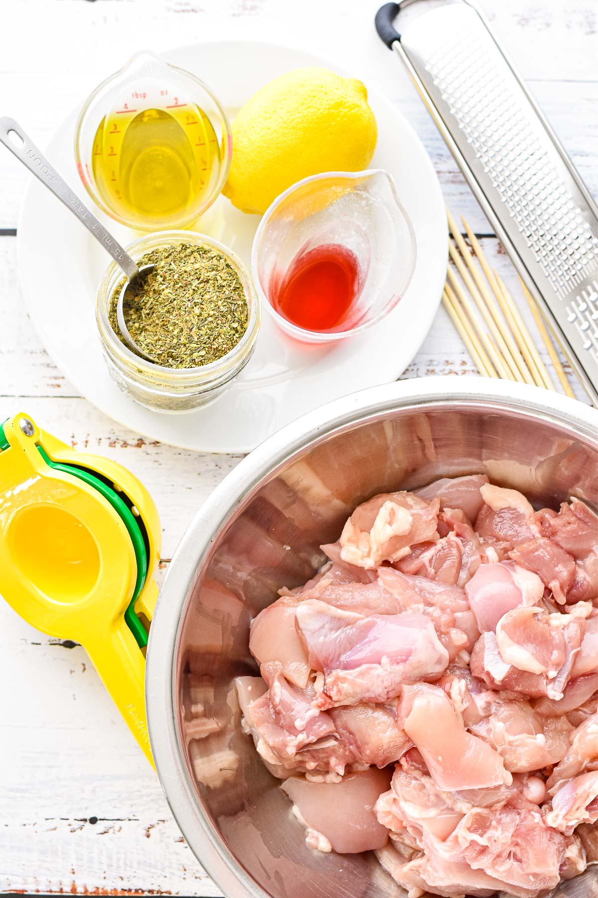 low fodmap chicken souvlaki ingredients including boneless skinless chicken thigh pieces, garlic infused olive oil, lemon juice and zest from a lemon, red wine vinegar, and low fodmap greek seasoning next to a citrus zester and juicer and wooden skewers