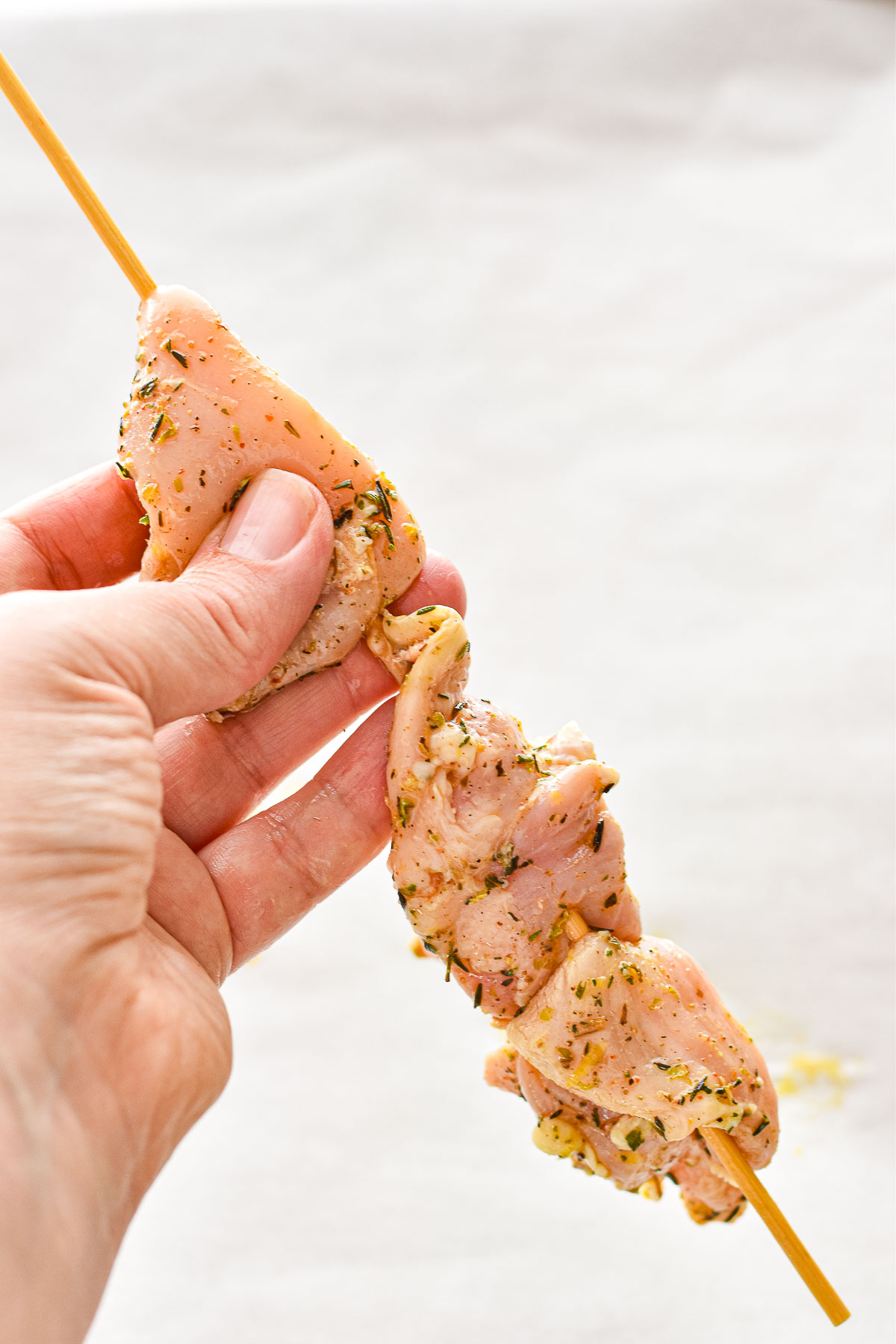 process shot of threading marinated chicken pieces onto a wooden skewer