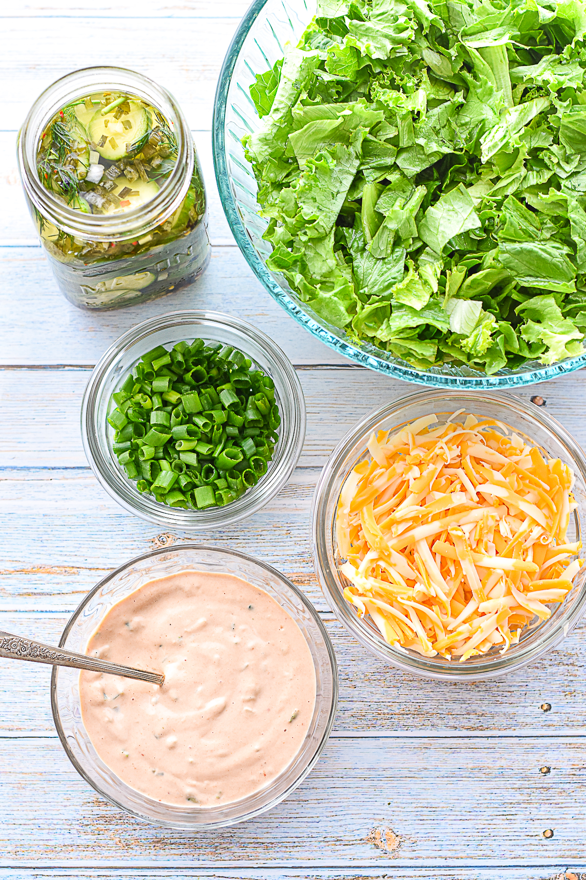 process shot of low FODMAP burger bowl produce and cheese ingredients, including chopped green leaf lettuce, low fodmap pickles, chopped scallions, shredded cheese next to a bowl of burger sauce for dressing
