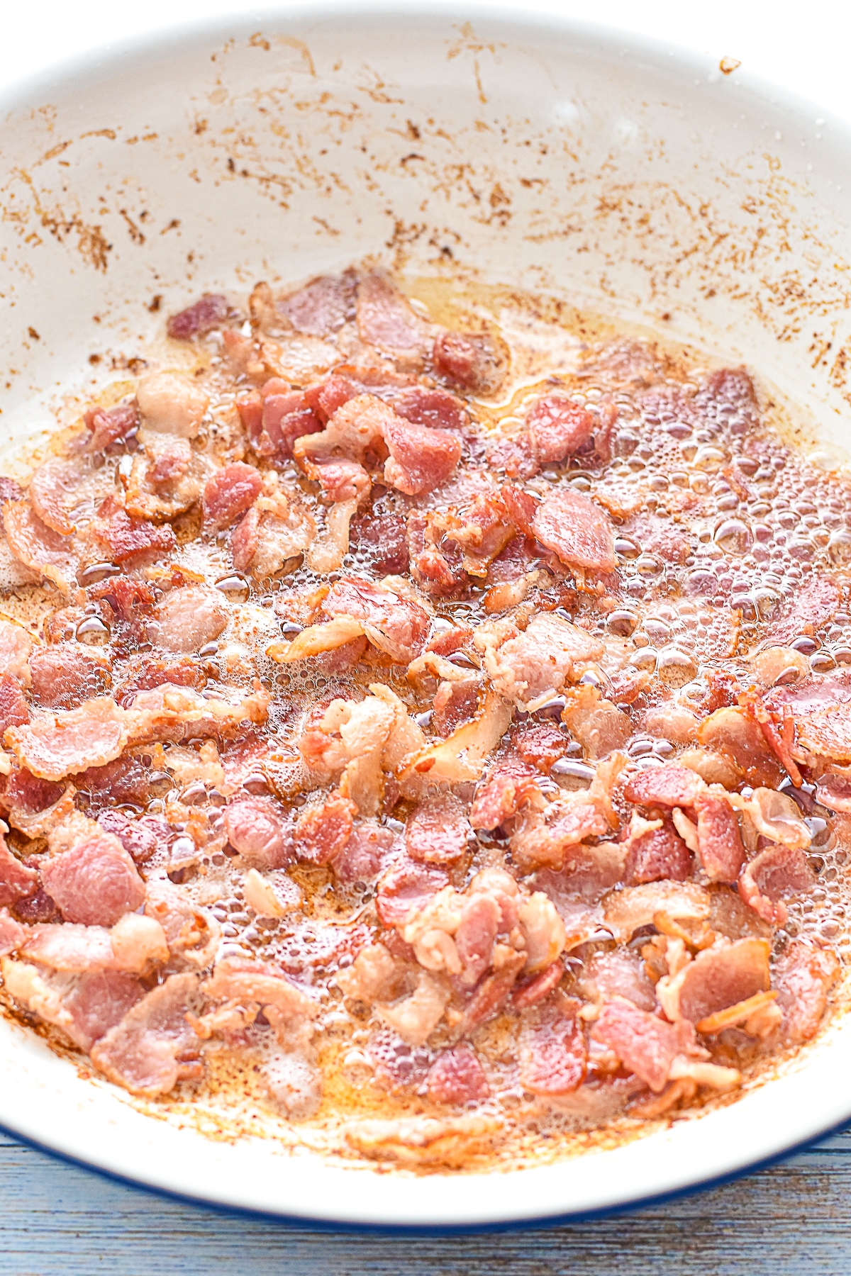 process shot of bacon pieces cooking in a large skillet