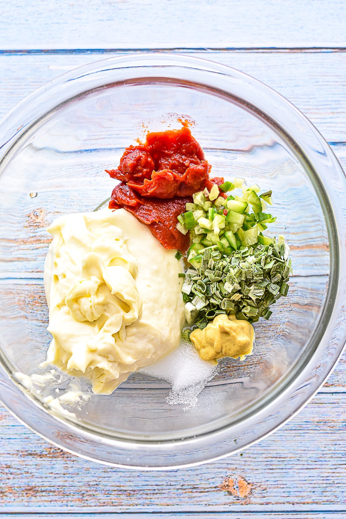overhead shot of low fodmap burger sauce ingredients in a glass bowl including mayo, tomato paste, finely chopped pickles, dried chives, dijon mustard, white vinegar, and liquid stevia