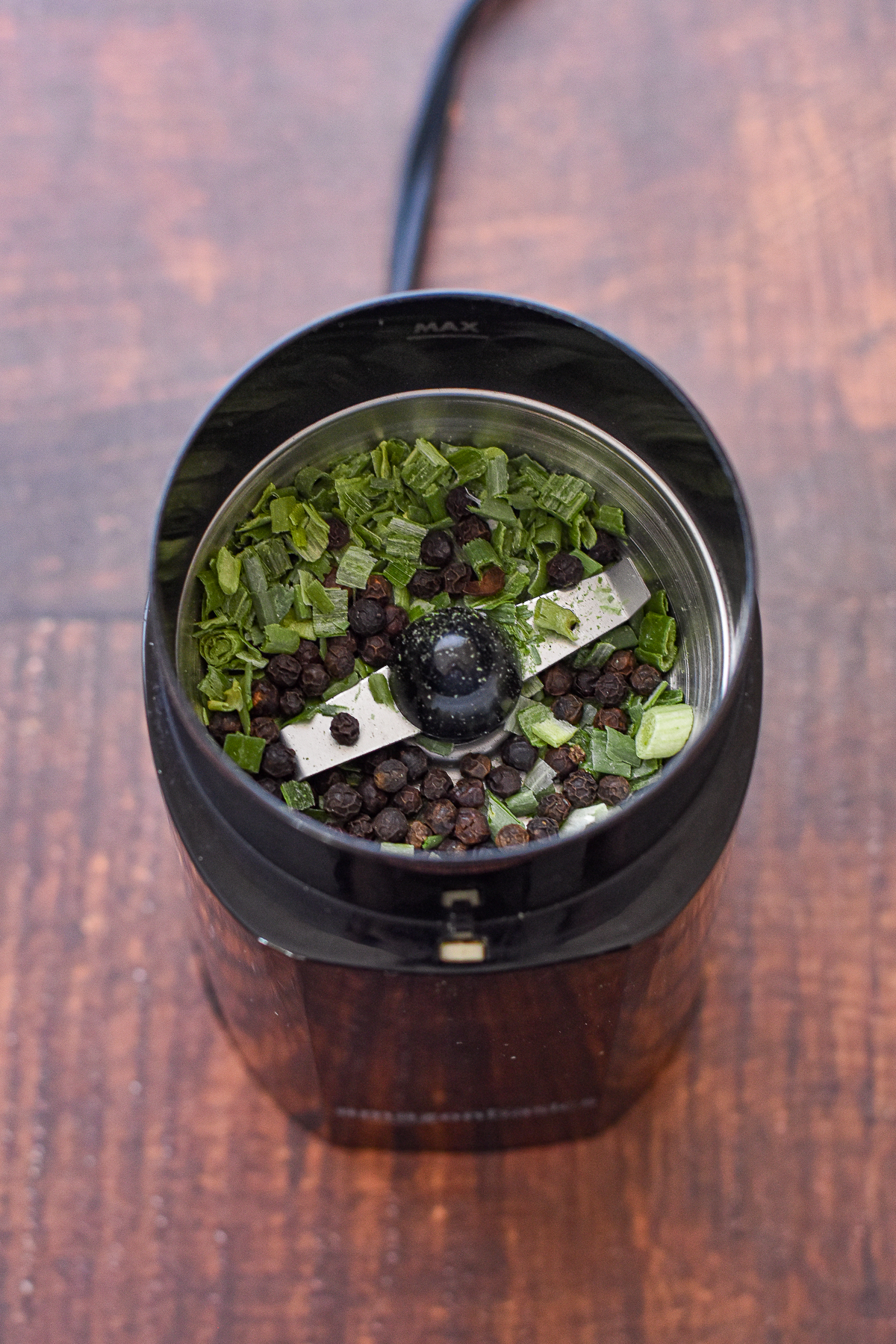 process shot of dried chives and whole peppercorns in an electric spice grinder prior to grinding