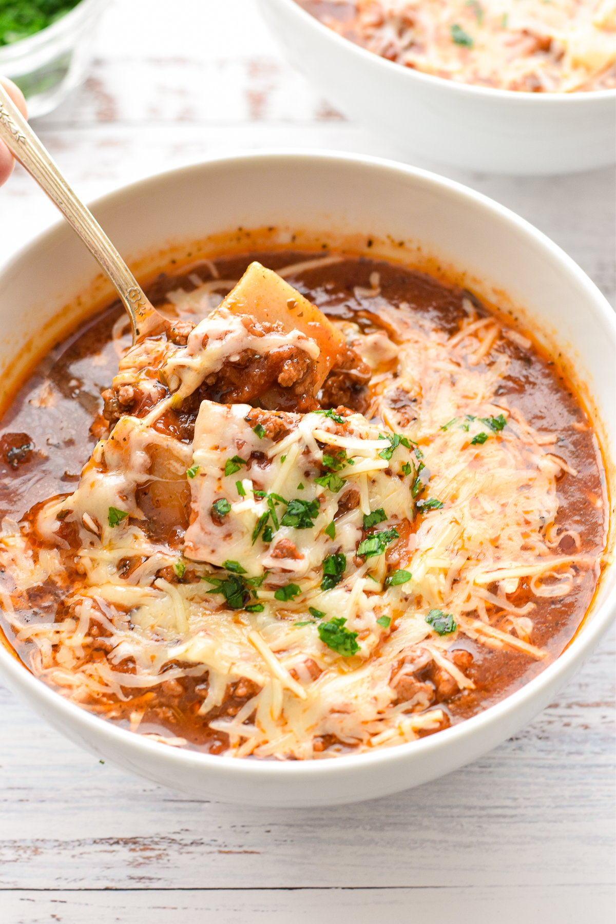 low fodmap lasagna soup scooped up by a spoon in a white bowl on a white background.