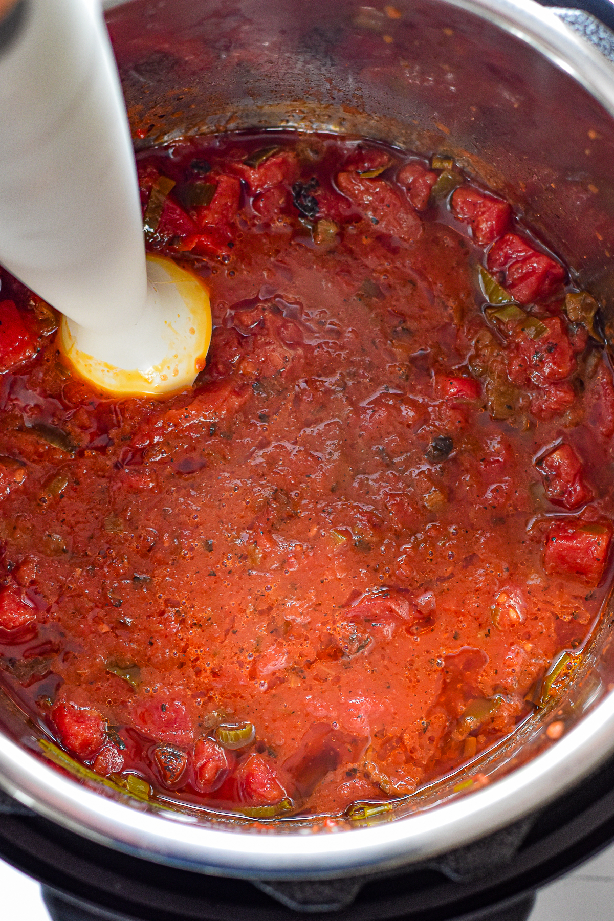 process shot of an immersion blender blending low fodmap marinara sauce in an instant pot after pressure cooking.