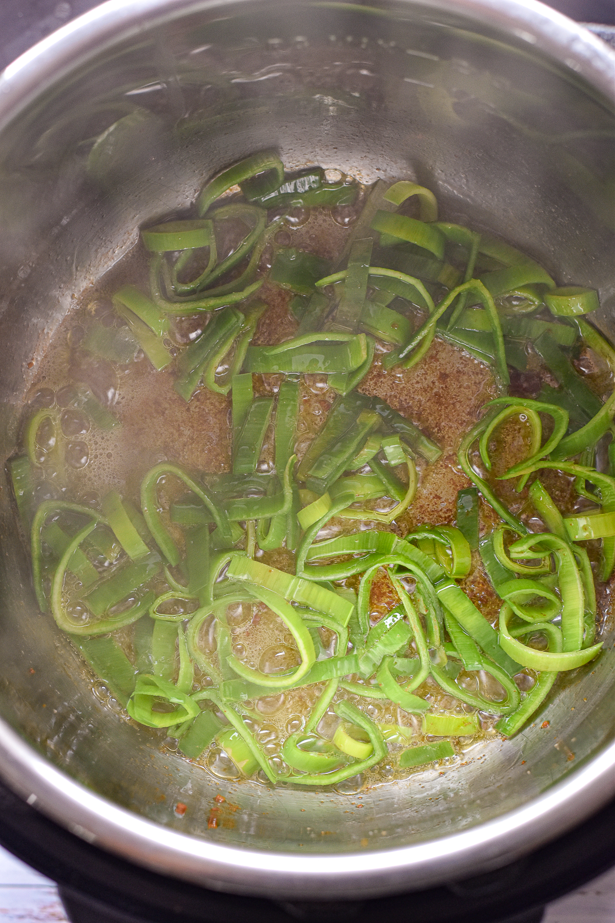 process shot of sliced leek greens sautéing in garlic-infused olive oil and bacon fat an Instant Pot.