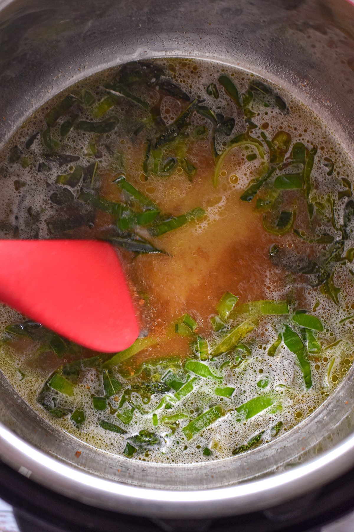 process shot of a spatula scraping the bottom in the Instant Pot after chicken broth is added to deglaze the pot.