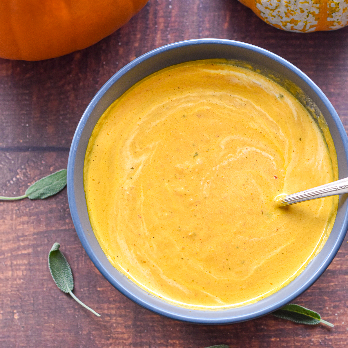 low fodmap pumpkin soup in a blue bowl with a spoon on a brown background.