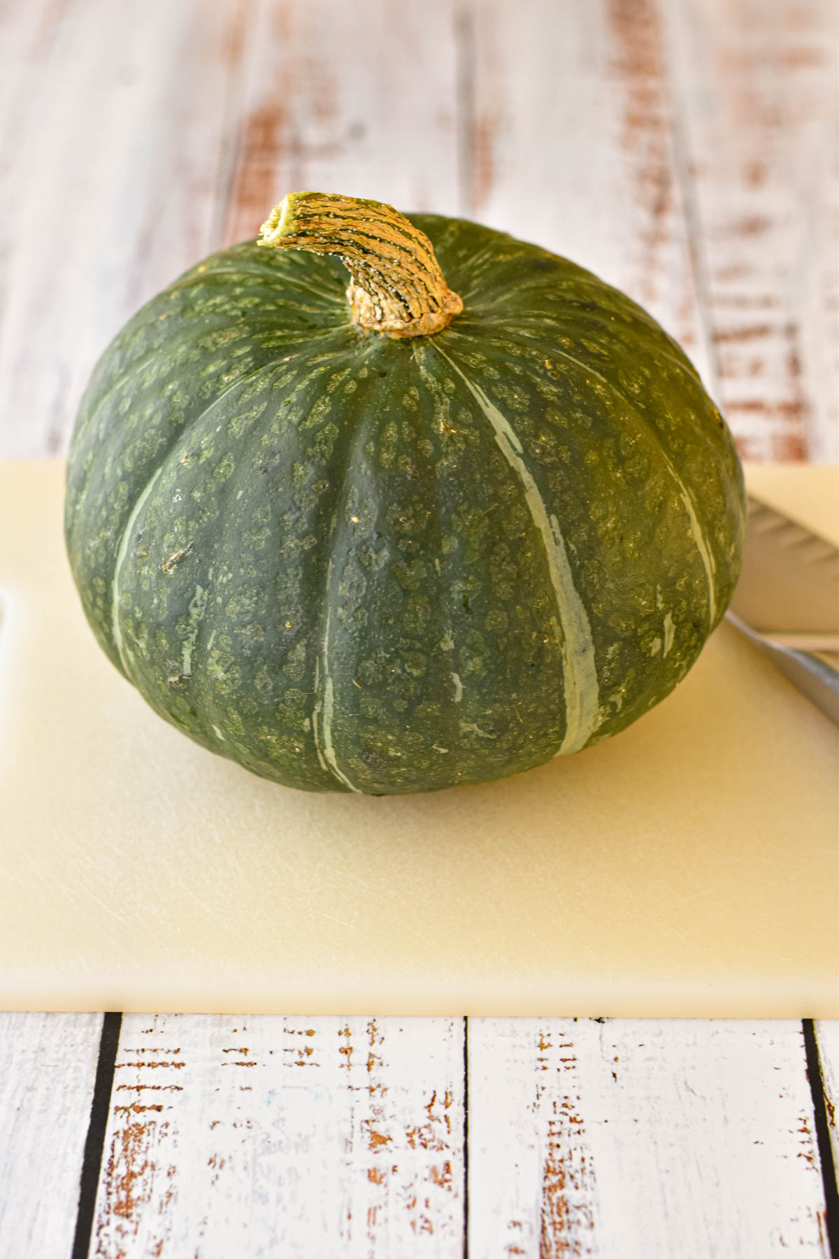 a kabocha squash / Japanese pumpkin on a white cutting board with a knife prior to chopping.