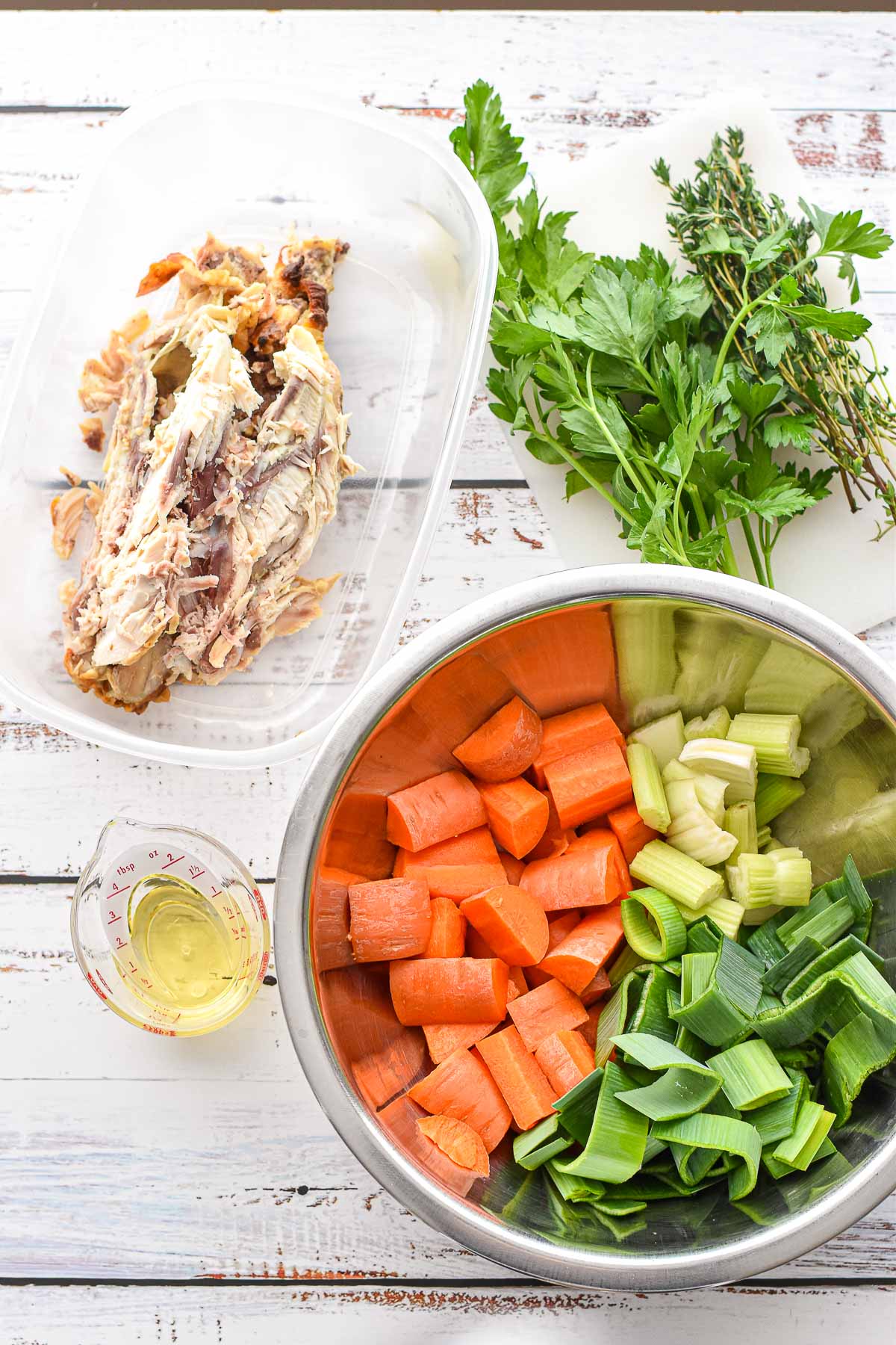 low fodmap chicken broth ingredients (photo 1 of 2) including a cooked chicken carcass, coarsely chopped carrots, celery, and leek greens, garlic-infused olive oil, and parsley and thyme sprigs.