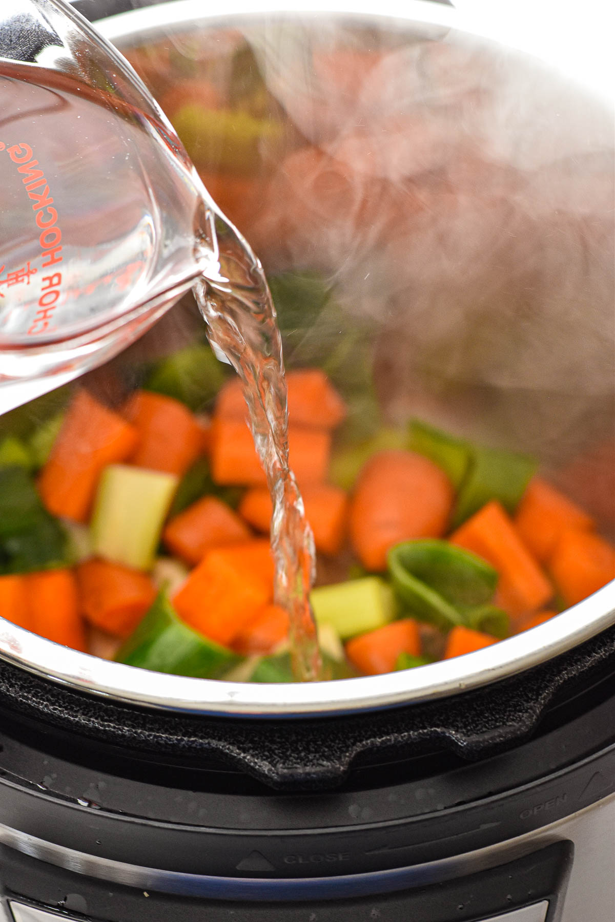 pouring water from a measuring cup into an instant pot with sautéing veggies to deglaze the pot.