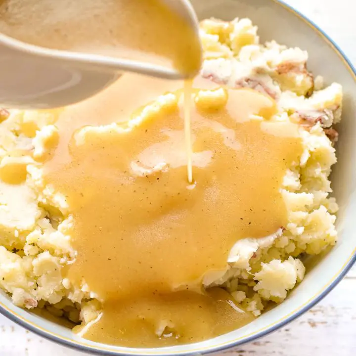 pouring low fodmap gravy from a gravy boat onto mashed potatoes in a bowl.