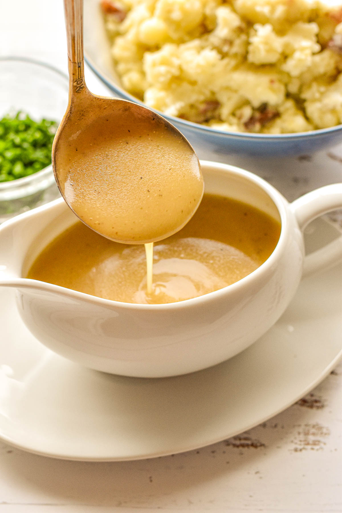 a ladle pouring low fodmap gravy into a gravy boat next to a bowl of mashed potatoes.