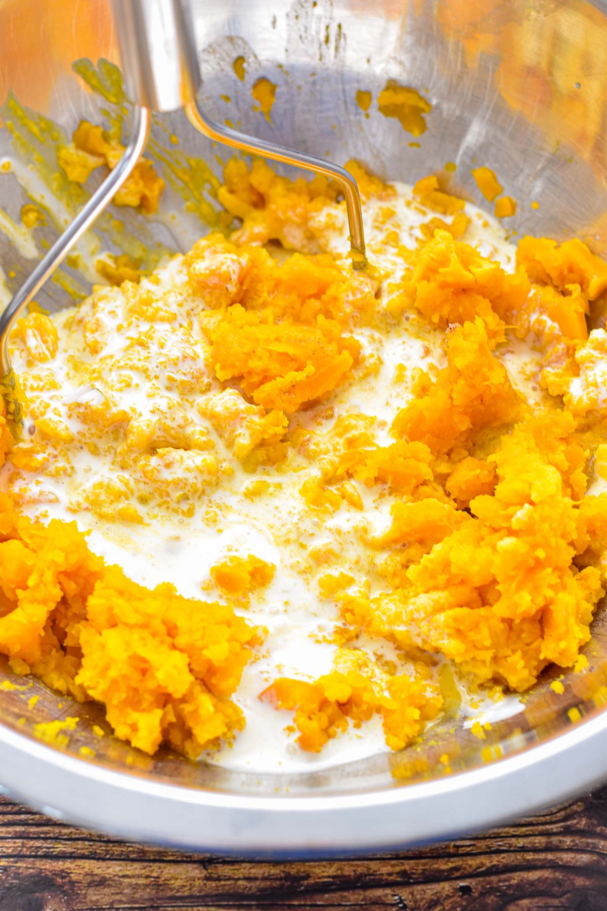 process shot of mashing squash topping ingredients in a large mixing bowl with a potato masher.