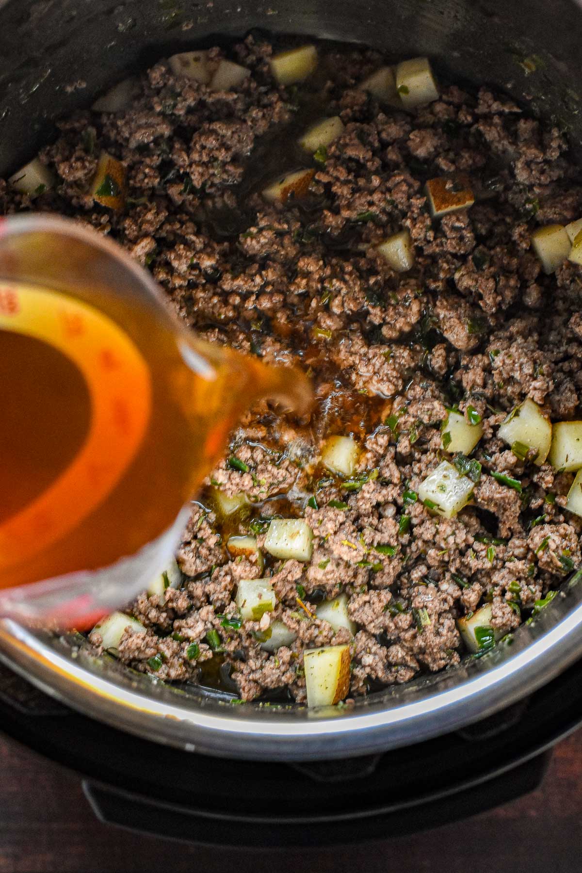pouring low fodmap beef broth into an instant pot to deglaze the pot containing low fodmap tourtiere filling.