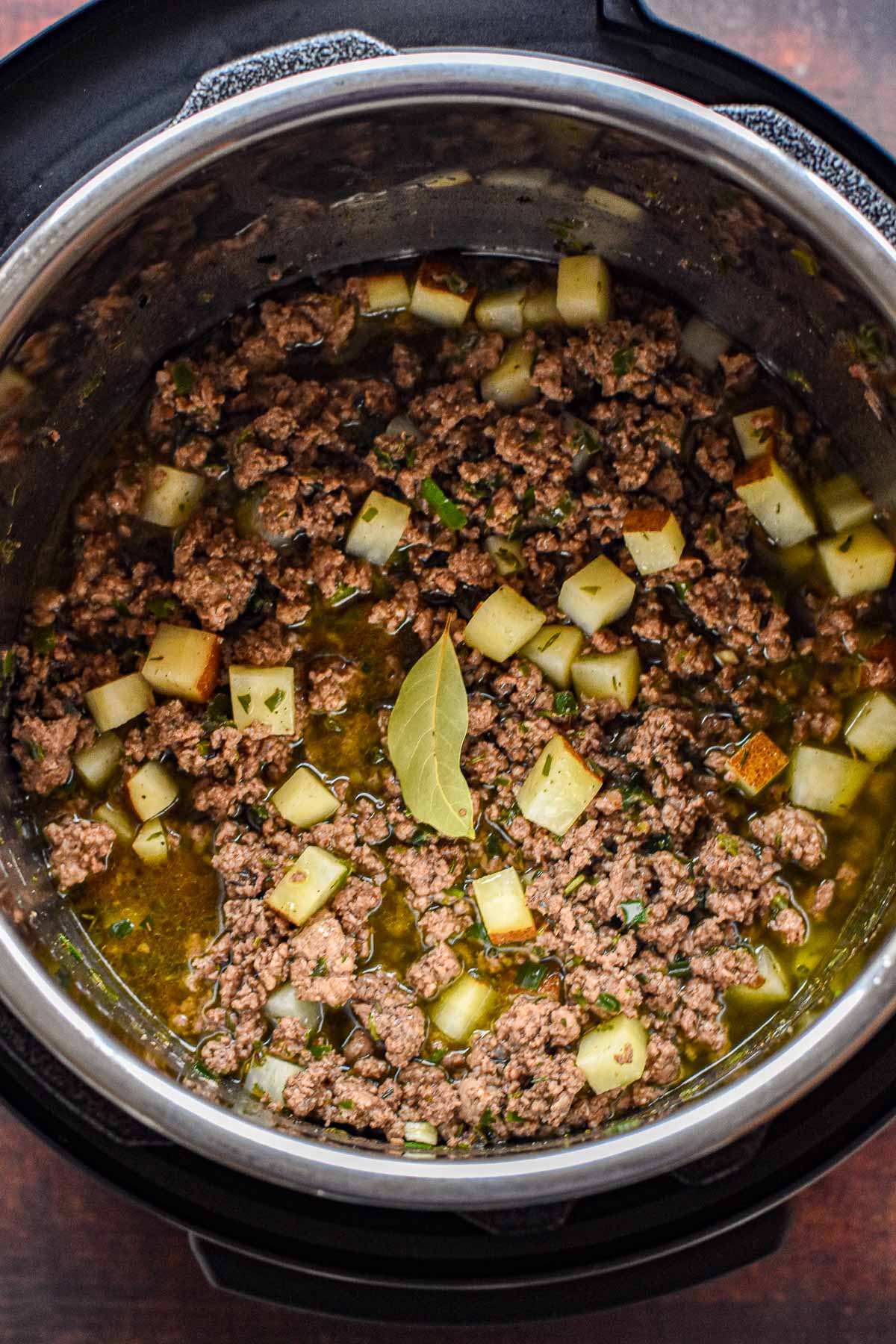 sauteed low fodmap tourtiere filling evenly distributed in an instant pot and topped with a bay leaf prior to pressure cooking.