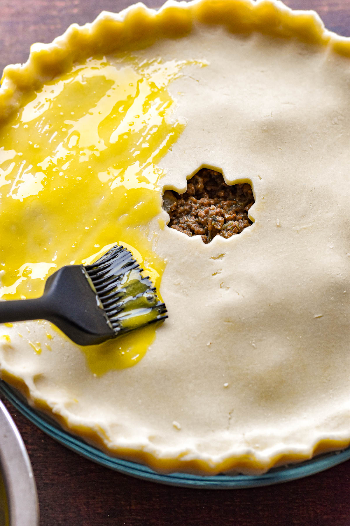 a basting brush applying egg yolk to the gluten-free crust of a low fodmap tourtiere prior to baking.
