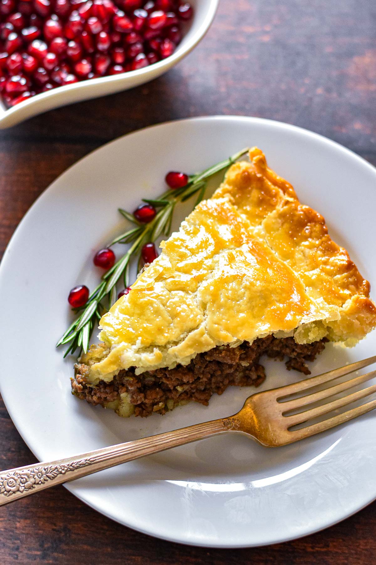 a piece of low fodmap tourtiere on a white plate with a fork and rosemary and pomegranate seed garnish.