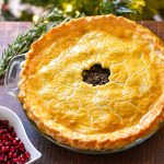 low fodmap gluten-free tourtiere with a maple leaf cut-out in the center of the crust on a wooden table in front of a christmas tree.
