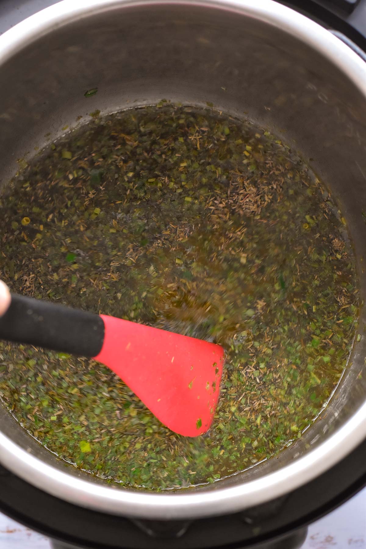 stirring seasonings into broth with a red spatula in an instant pot.
