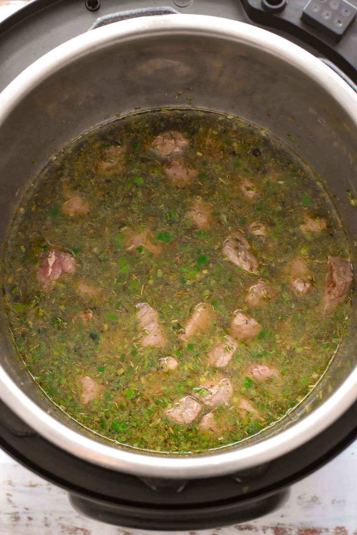 overhead shot after beef stew meat is added to seasoned broth prior to adding the vegetables in an instant pot.