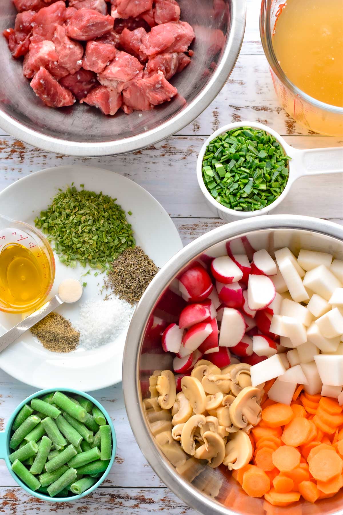 keto beef stew ingredients including chopped beef stew meat, beef broth, finely chopped leek greens, chopped radish and turnip, sliced carrot and canned mushrooms, frozen cut green beans, dried chives and thyme, kosher salt, ground black pepper, garlic-infused olive oil, and xanthan gum (optional).