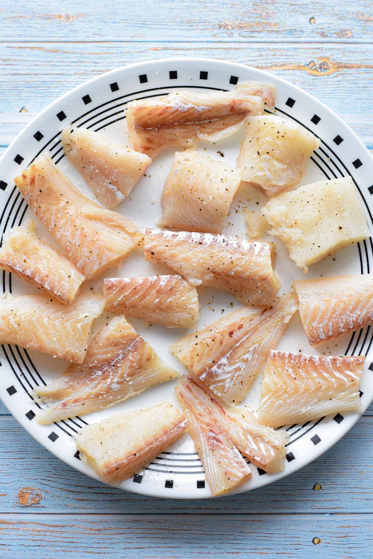 chopped white fish fillets seasoned with sea salt and ground black pepper on a black and white plate.