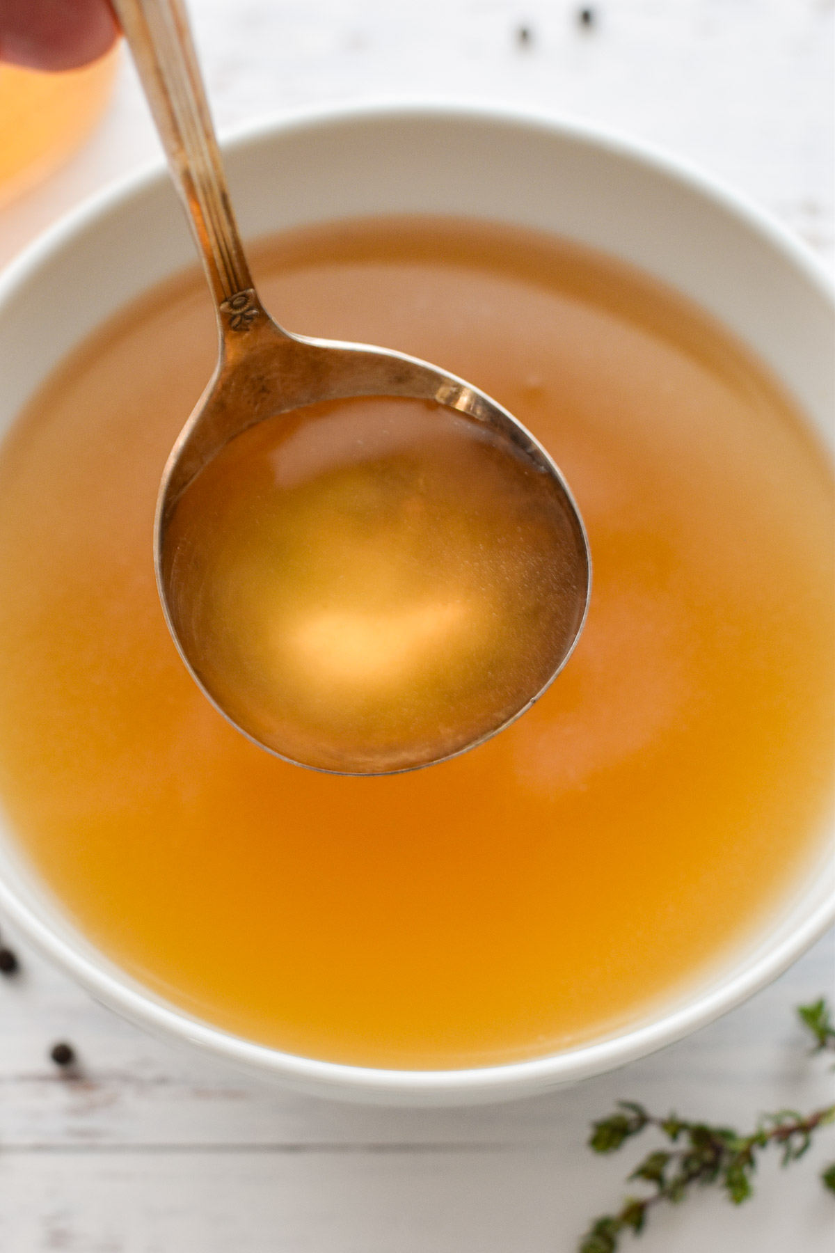 a ladle of low fodmap bone broth over a white bowl of broth.
