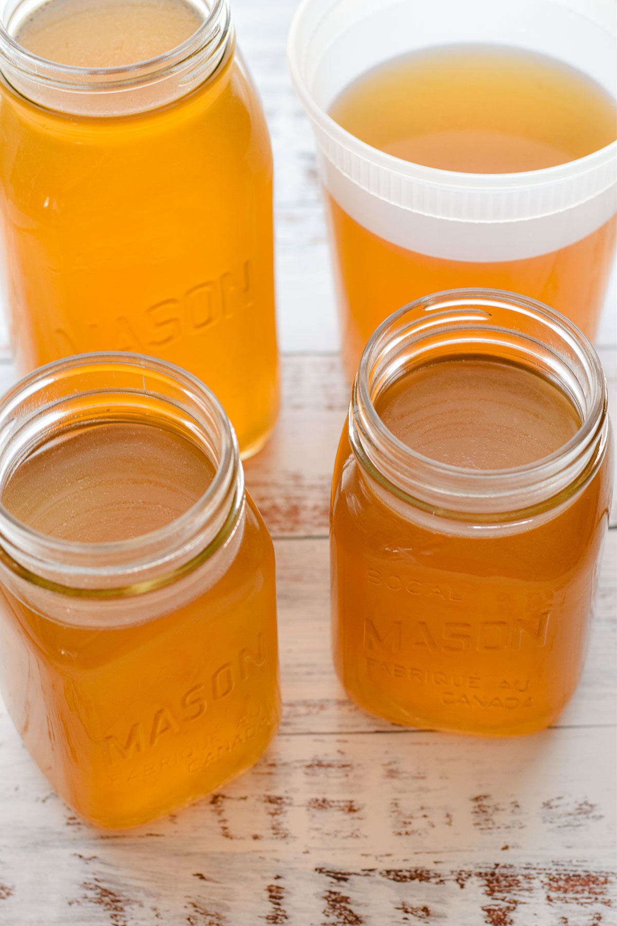 low fodmap beef bone broth in mason jars and a deli container cooling on a white table.