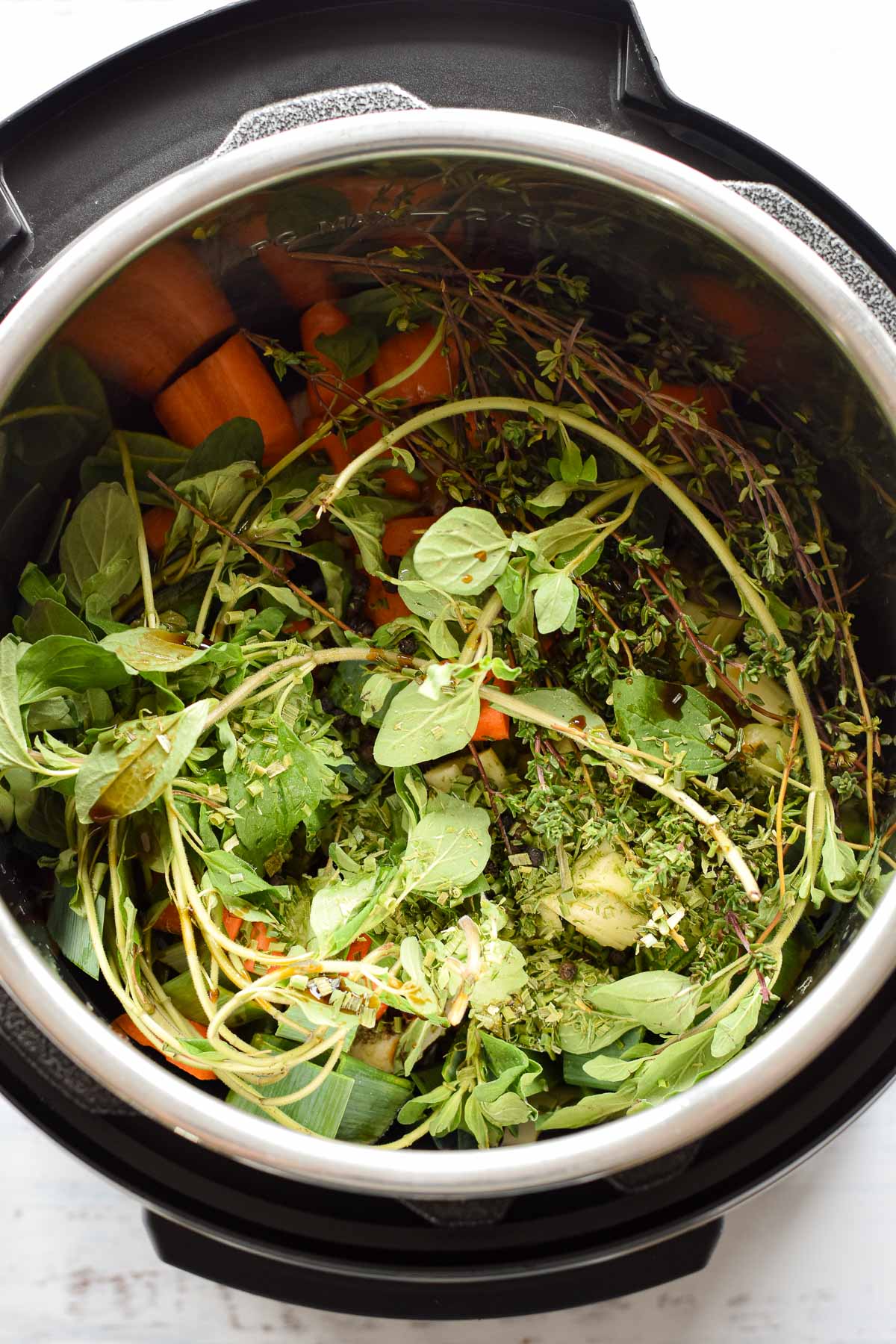 overhead shot of the instant pot once herbs, seasonings, and produce have been added to make low fodmap beef broth.