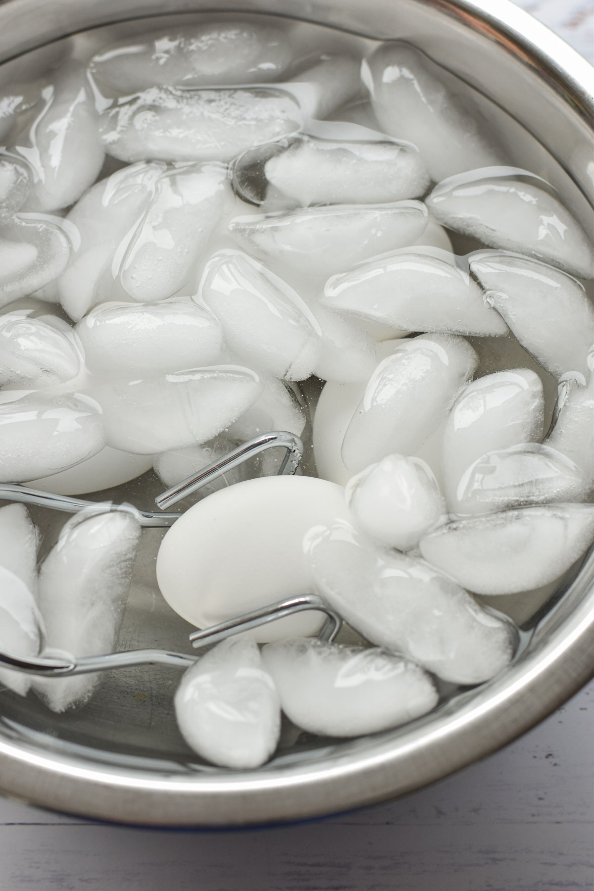 tongs adding a hard boiled egg to an ice bath for cooling.