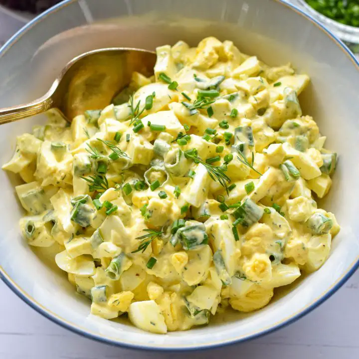 instant pot egg salad garnished with chives and dill in a blue and white bowl with a spoon.